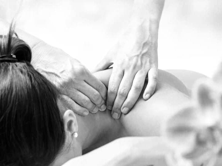 Black and white close-up of hands massaging a person's neck and shoulders for relaxation.