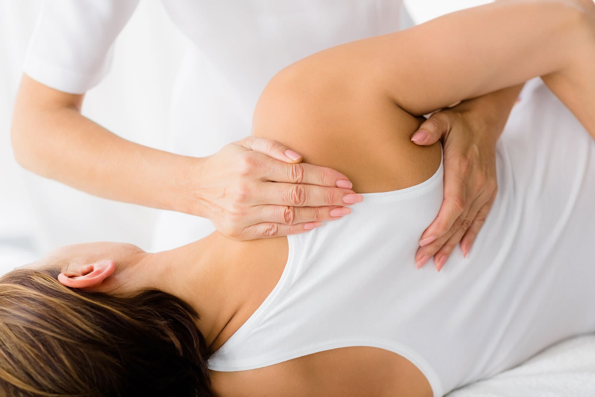 Therapist's hands performing shoulder and upper back massage on a patient.